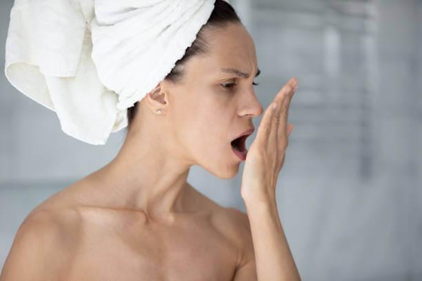 a woman smelling her breath, looking concerned.