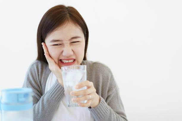 A woman holding her cheek in discomfort, experiencing tooth sensitivity.