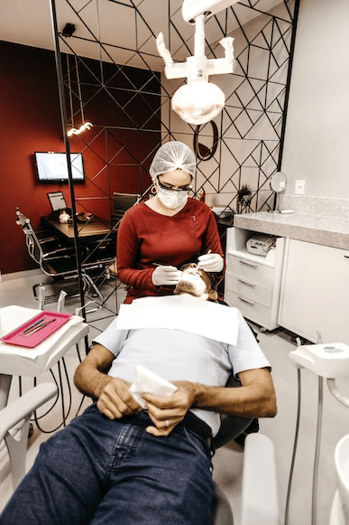 a dentist in red scrubs performing a dental procedure on her patient