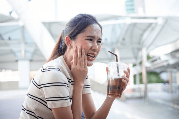 a woman drinking iced coffee experiencing tooth sensitivity